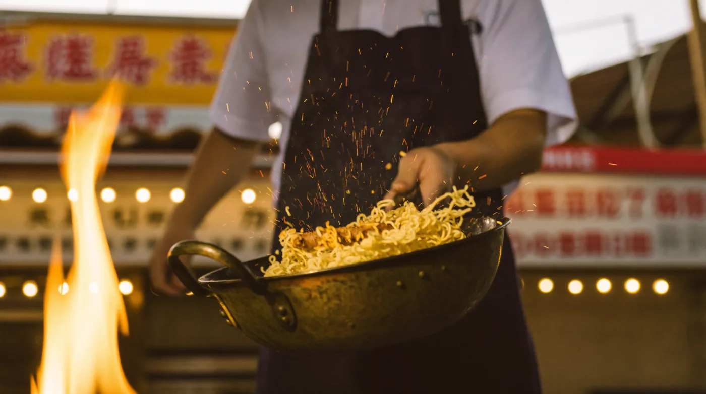 Street cook working a wok over high flame at a Yaowarat stall in Bangkok Chinatown