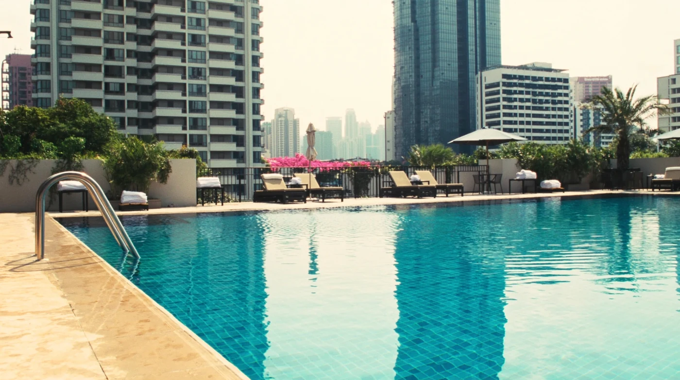Hotel pool with loungers and parasols under a bright Bangkok midday sky