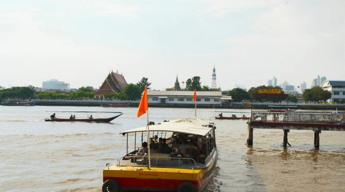 Orange flag Chao Phraya express boat arriving at a wooden pier in Bangkok