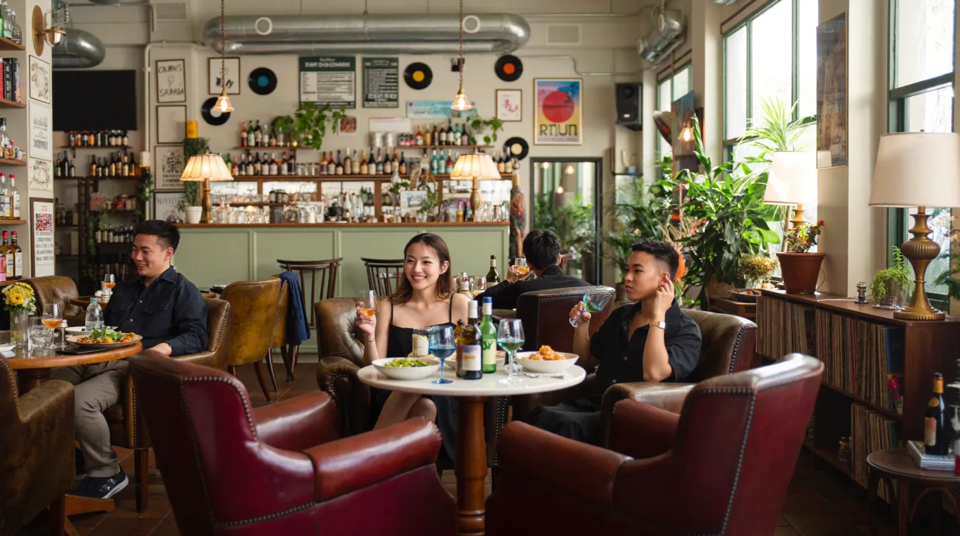 Friends over drinks among vintage armchairs and warm lamps at an Ekkamai bar restaurant in Bangkok