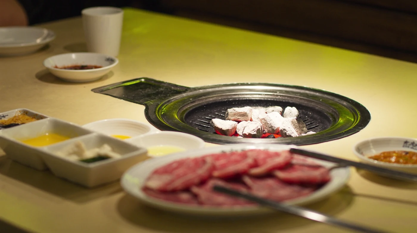 Charcoal grill set into a table with marbled sliced beef and banchan dishes
