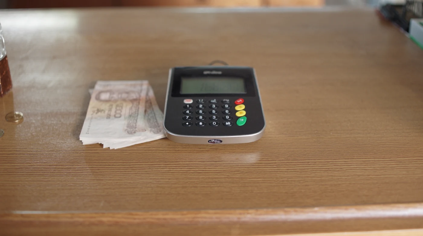 Card payment terminal on a cafe counter in Bangkok with baht notes beside it