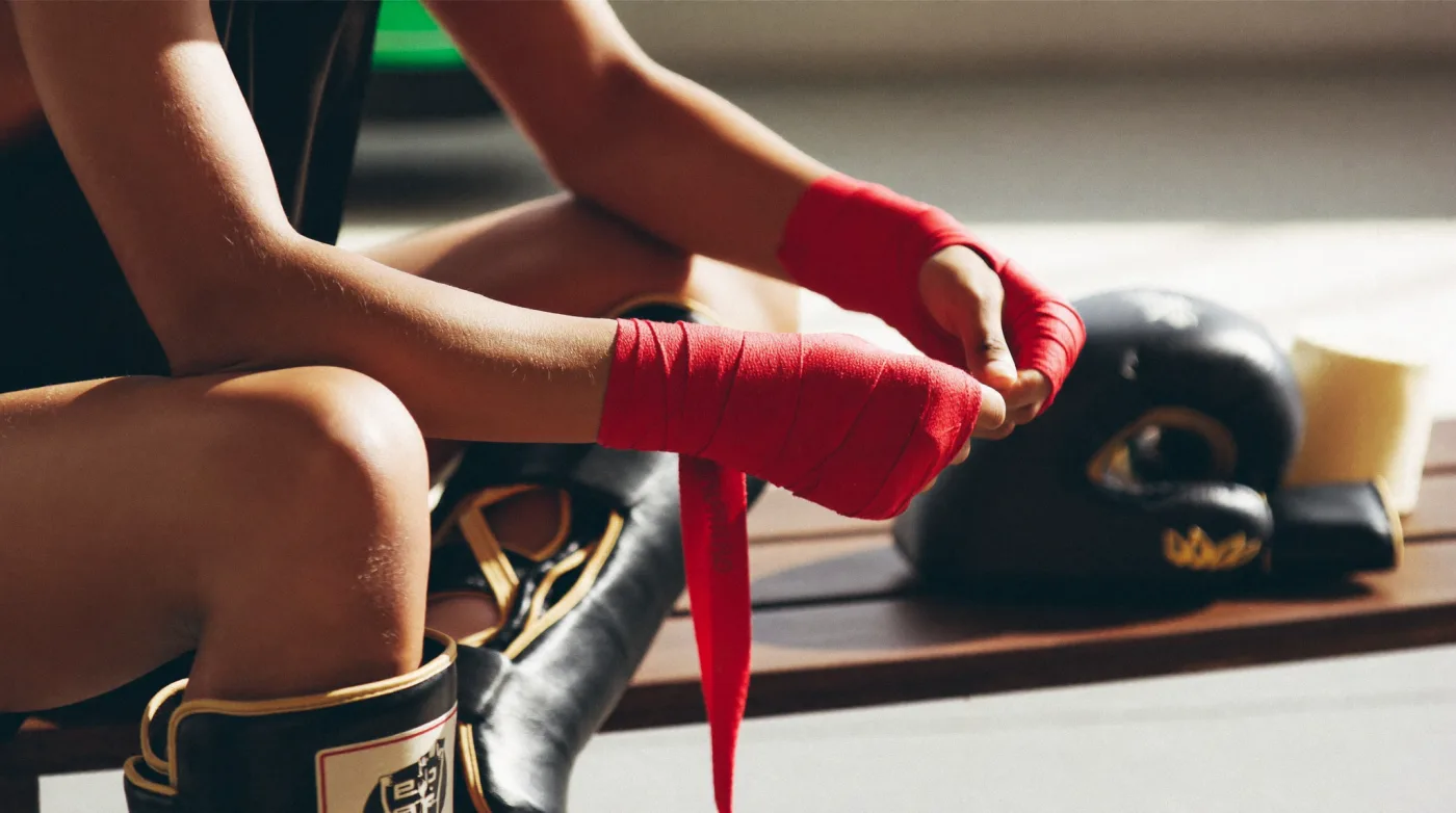 Fighter wrapping their hands beside gloves and shin guards on a bench in a Muay Thai gym