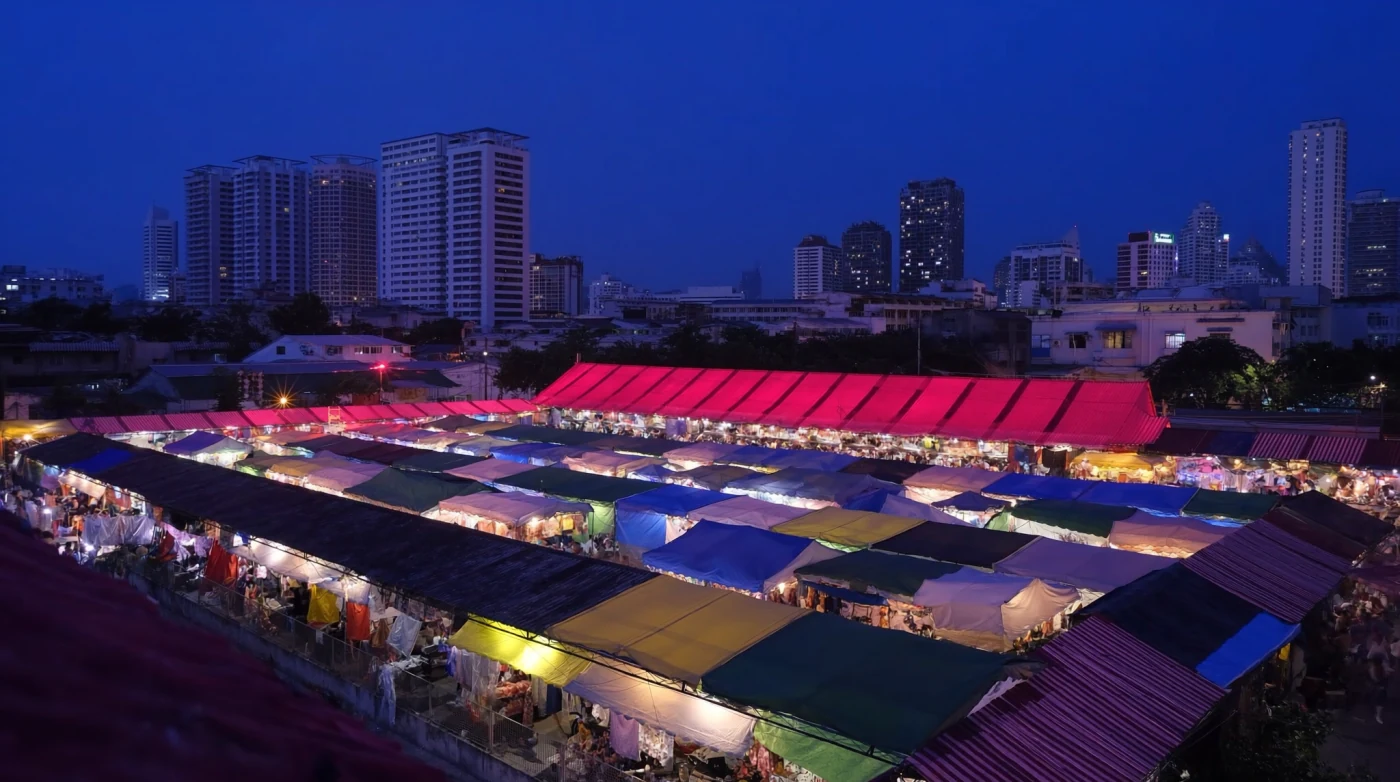 Colourful canopy tents and crowds at a Bangkok night market beside a lit office tower