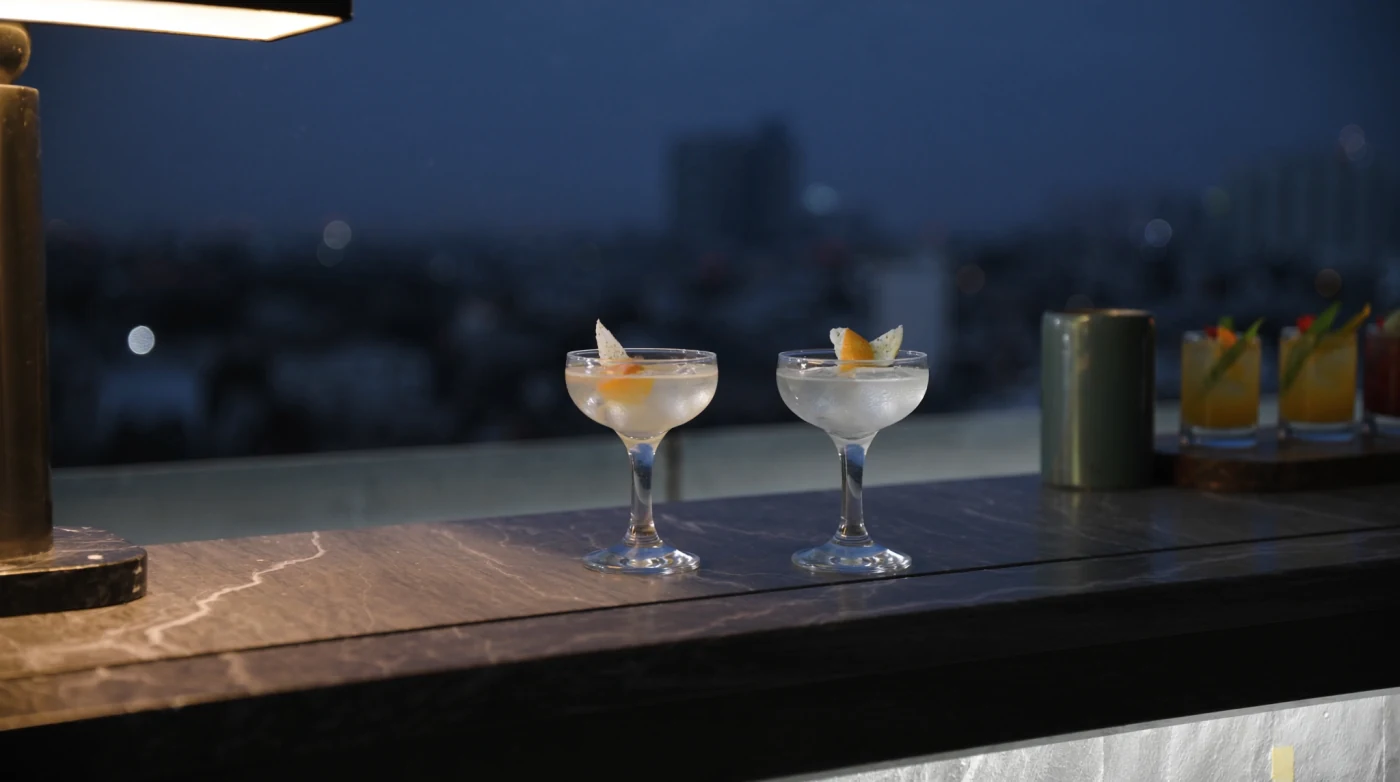 Cocktail glass on a rooftop bar table with city lights out of focus behind