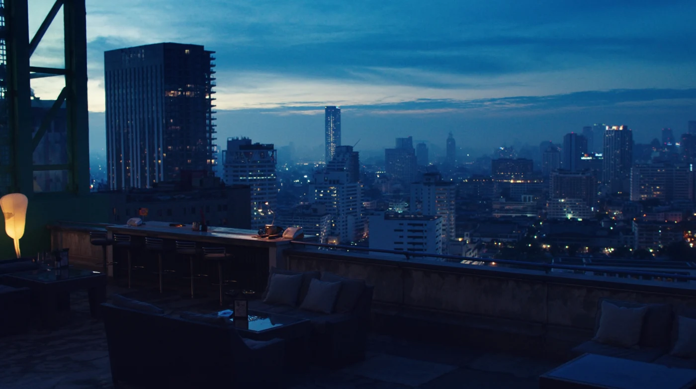 Rooftop bar counter at blue hour with the lit Bangkok skyline behind it